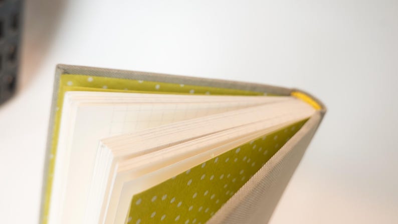 May include: Open notebook with lined pages. The cover is a light gray fabric with a yellow and white polka dot pattern on the inside cover. The spine is yellow.