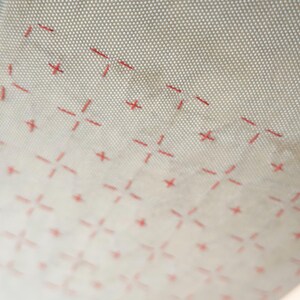 May include: Close-up of a beige, flexible baking mat with a grid pattern and red cross-shaped markings. The mat is rolled up slightly, revealing its texture and design. The pattern is evenly spaced.