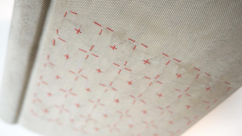 May include: Close-up of a beige, flexible baking mat with a grid pattern and red cross-shaped markings. The mat is rolled up slightly, revealing its texture and design. The pattern is evenly spaced.