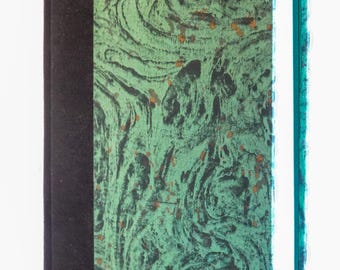 May include: A hardcover book with a black spine and a green and black marbled cover. The cover has a swirling pattern with small flecks of gold. The pages are white, and the edges are teal.