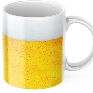 Può includere: Tazza in ceramica bianca con un design di un bicchiere di birra con una testa di schiuma e condensa all'esterno.