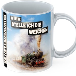 May include: White ceramic mug with a black and white image of a steam train with the text "HIER STELLE ICH DIE WEICHEN" and "FAHRDIENSTLEITER" on the side.