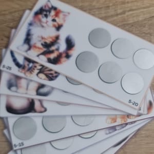 Puede incluir: Un conjunto de seis tarjetas blancas con una ilustración de un gato y una fila de seis círculos plateados en cada tarjeta. Las tarjetas están etiquetadas con números: 6-26, 5-20, 5-15.