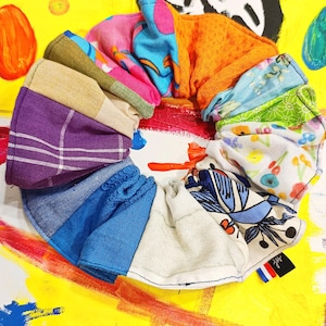 Peut inclure: Un chouchou en tissu circulaire multicolore, avec divers motifs et textures. Le chouchou présente des sections bleues, violettes, oranges et à motifs floraux. Le fond est jaune vif avec de l'art abstrait.