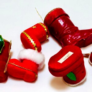 May include: A collection of red Christmas ornaments, including boots and heart-shaped boxes. Some ornaments have gold trim, holly accents, and white faux fur. The ornaments are labeled "JAPAN".