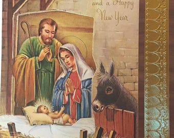 Op de afbeelding: Een vintage kerstkaart met een afbeelding van de kerststal met Maria, Jozef en baby Jezus in een kribbe. De kaart heeft een gouden rand en de tekst "A Blessed Christmas and a Happy New Year".