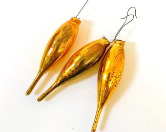 Op de afbeelding: Drie gouden glazen kerstversieringen met een puntige punt en een draadhanger. De ornamenten zijn een vintage kerstversiering.