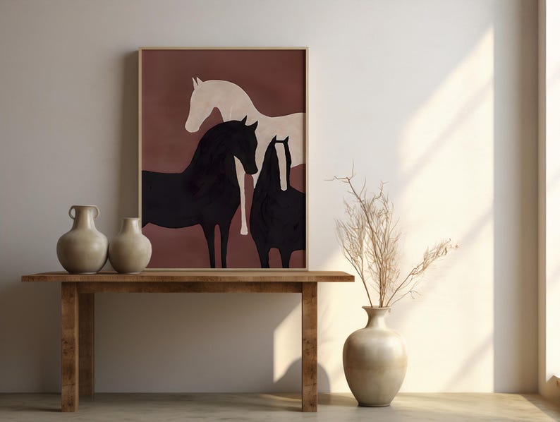 K&ouml;nnte beinhalten: Gerahmter Kunstdruck mit drei stilisierten Pferden in Schwarz und Creme vor einem rotbraunen Hintergrund. Das Kunstwerk wird &uuml;ber einem Holztisch mit zwei beigen Vasen pr&auml;sentiert. Eine Vase mit getrockneten Zweigen steht daneben.