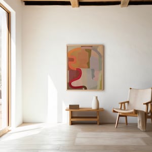 Puede incluir: Una pieza de arte mural rectangular en un marco de madera clara con formas abstractas en tonos naranja, rojo, marrón, rosa y gris. Debajo del arte hay un banco de madera con una pila de libros y un jarrón de cerámica blanca junto a una silla.