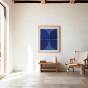 Pode incluir: Uma impressão de arte emoldurada com quatro segmentos circulares azul-escuros dispostos em grelha. A obra está exposta numa parede branca sobre um banco de madeira com uma pilha de livros e um vaso branco, ao lado de uma cadeira de madeira clara.