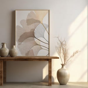 May include: A wooden table with two beige vases and a framed artwork featuring a botanical design. The artwork displays a stylized illustration of leaves in shades of beige and brown. A vase with dried branches is on the right.
