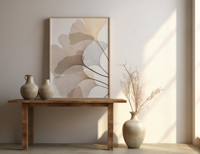 May include: A wooden table with two beige vases and a framed artwork featuring a botanical design. The artwork displays a stylized illustration of leaves in shades of beige and brown. A vase with dried branches is on the right.