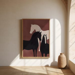 May include: A framed wall art print featuring a deep terracotta background with three horses. One horse is light cream, while the other two are solid black, with one of the black horses displaying a distinct white vertical stripe on its face.