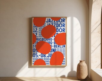 May include: A rectangular framed poster featuring a white background with repeating blue text that reads JAZZDOR STRASBOURG-BERLIN and 05.-08. JUNI 2018. Large, solid orange organic shapes are layered over the text, partially obscuring the blue lettering.