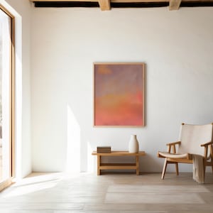 May include: A bright, airy interior space with a large window and a framed abstract painting. A wooden bench holds a white vase and a stack of books. A wooden chair with a cream-colored throw completes the scene.