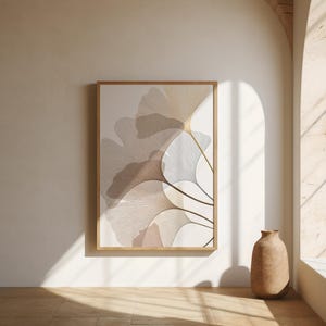 May include: A framed art print featuring a botanical design of stylized ginkgo leaves in shades of beige, brown, and white. The artwork is displayed on a white wall, with a wooden frame. A decorative vase sits on the floor.