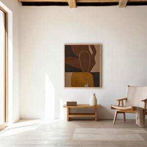 Puede incluir: Interior luminoso con una gran ventana y una obra de arte abstracta enmarcada en madera. Un pequeño banco de madera sostiene un jarrón blanco y libros. Una silla de madera con asiento crema y una manta completan la escena.