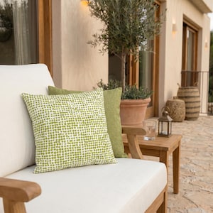 May include: Outdoor seating arrangement featuring a white cushion sofa with two decorative pillows. One pillow has a white background with green dot pattern, the other is solid green. A wooden side table holds a lantern and a glass of water.
