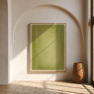 May include: A rectangular wall art piece featuring a solid olive green center bordered by a thin cream-colored margin, all enclosed within a light-toned wooden frame. The artwork is displayed on a plain wall, capturing a simple, clean aesthetic.
