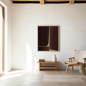 以下が含まれることがあります： 茶色とベージュの色合いの抽象的なアートワークが額装された、ミニマリストなインテリア。木製のベンチには白い花瓶と本が置かれています。クリーム色の座面と毛布が付いた木製の椅子が部屋を完成させています。