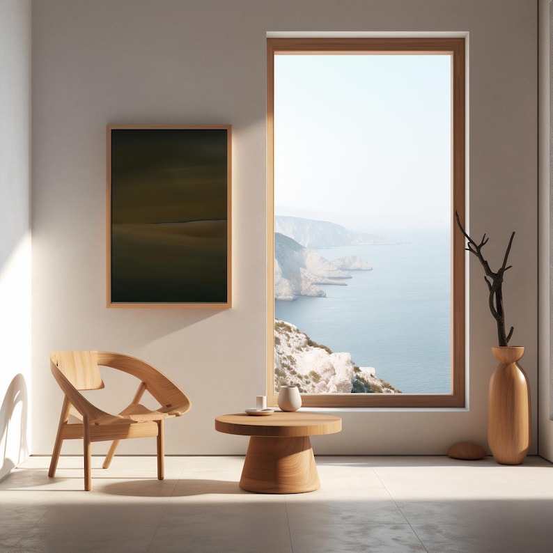 May include: A minimalist interior scene featuring a wooden chair, a small round table, and a tall vase with a branch. A framed landscape painting hangs on the wall. A large window offers a view of the ocean and cliffs.