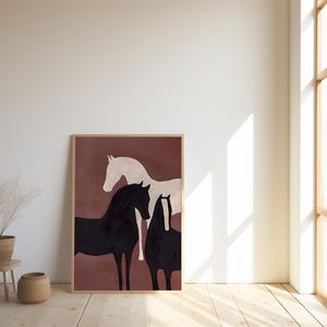 K&ouml;nnte beinhalten: Ein gerahmter Kunstdruck mit drei stilisierten Pferden in Schwarz und Wei&szlig; vor einem ged&auml;mpften rotbraunen Hintergrund. Das Kunstwerk wird in einem hellen Holzrahmen pr&auml;sentiert und verleiht der Raumdekoration einen Hauch von rustikaler Eleganz.