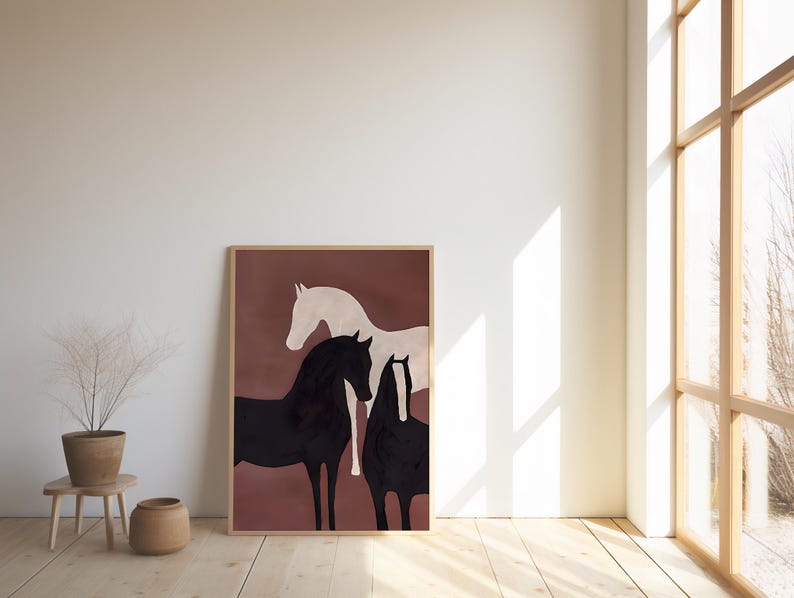 K&ouml;nnte beinhalten: Ein gerahmter Kunstdruck mit drei stilisierten Pferden in Schwarz und Wei&szlig; vor einem ged&auml;mpften rotbraunen Hintergrund. Das Kunstwerk wird in einem hellen Holzrahmen pr&auml;sentiert und verleiht der Raumdekoration einen Hauch von rustikaler Eleganz.