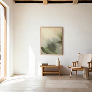 May include: A light-filled room featuring a large window and a framed abstract artwork. A wooden bench holds a vase and books, and a wooden chair with a cream-coloured throw is nearby. The room has a minimalist, natural aesthetic.