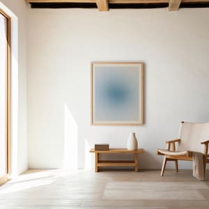 Puede incluir: Interior luminoso y espacioso con una gran ventana y una obra de arte enmarcada. Una pequeña mesa de madera sostiene un jarrón blanco y libros. Una silla de madera con asiento crema y una manta está en la esquina.