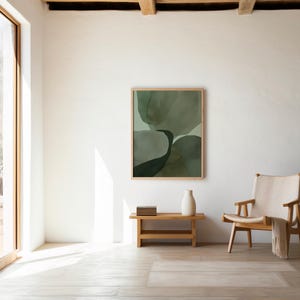 May include: A framed rectangular wall art piece featuring abstract, layered organic shapes in varying shades of sage, olive, and dark forest green. The artwork is displayed in a light-toned wooden frame, showcasing soft, blended colour transitions.