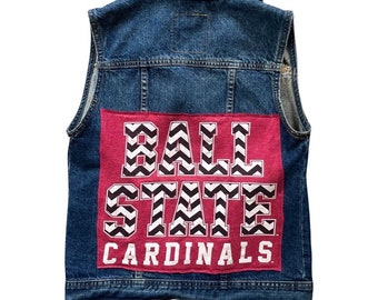 May include: A blue denim vest with a red patch on the back. The patch has a black and white chevron pattern and the text "BALL STATE CARDINALS".