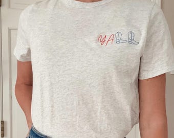 May include: A gray t-shirt with the word "Y'ALL" embroidered in red and blue thread. The word is accompanied by two blue embroidered cowboy boots.