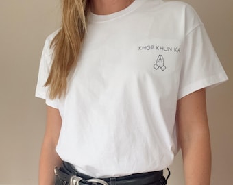May include: White t-shirt with the text "Khop Khun Ka" and a graphic of two hands clasped in prayer.