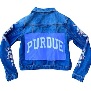 May include: A blue denim jacket with floral embroidery on the sleeves and a blue patch on the back that says "PURDUE" in white letters.