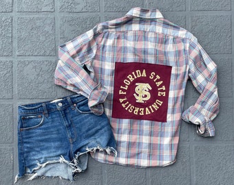 May include: A blue and pink plaid flannel shirt with a maroon patch on the back that says "Florida State University".