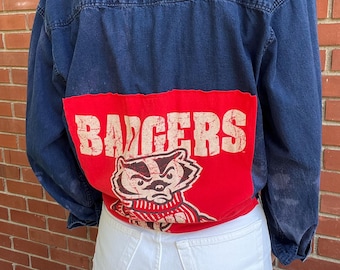 May include: A blue denim jacket with a red patch on the back. The patch features a cartoon badger wearing a striped scarf and the word "BADGERS" in white lettering.