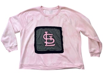 May include: A pink sweatshirt with a gray and black patch featuring a pink "St. Louis" logo.