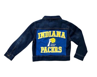 May include: A blue denim jacket with a blue and yellow Indiana Pacers patch on the back. The patch features the team's logo and the words "Indiana Pacers".