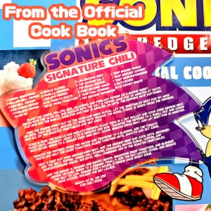 May include: A recipe card from the official Sonic the Hedgehog cookbook, featuring a recipe for Sonic's Signature Chili. The card has a purple and pink design with the Sonic logo and a picture of Sonic's shoe.