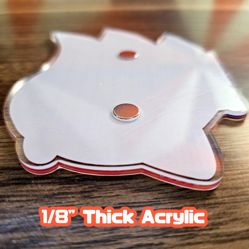 May include: A clear acrylic piece with a white interior and red trim, featuring two small, round, copper-coloured accents. The text "1/8" Thick Acrylic" is displayed in orange letters.