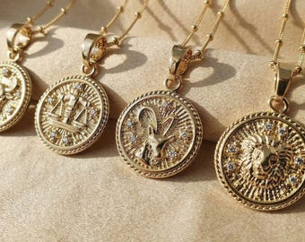 May include: Four gold-toned necklaces featuring circular pendants with raised zodiac symbols, including Libra and Leo, surrounded by small embedded clear stones. Each pendant hangs from a delicate gold chain with a textured rope-style border.