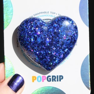 May include: A blue heart-shaped phone grip with glitter embedded in the resin. The grip is labeled "POPGRIP" on the packaging.