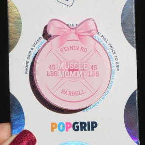 May include: Pink phone grip with a pink bow and a weight plate design. The weight plate says "Standard" and "45 LBS Muscle Mommy LBS Barbell".
