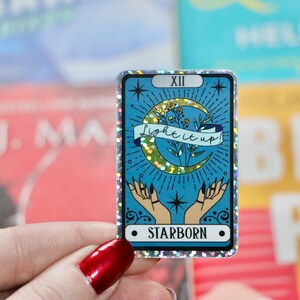 Pu&ograve; includere: Un adesivo olografico con sfondo blu e una luna crescente dorata. L'adesivo presenta una mano con una luna crescente e il testo "Light it up!" e "Starborn".