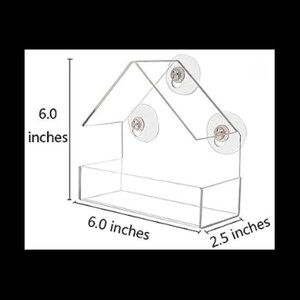 May include: A clear plastic bird feeder shaped like a house with three suction cups. The feeder measures 15.2 cm wide, 15.2 cm tall, and 6.4 cm deep.