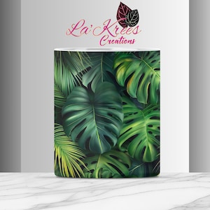 Pode incluir: Uma caneca de cerâmica branca com um design de folhas tropicais. O design apresenta grandes folhas verdes sobre um fundo verde escuro.