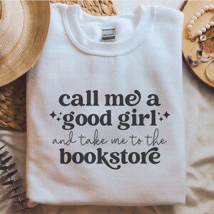 May include: White sweatshirt with black text that reads 'Call me a good girl and take me to the bookstore'.