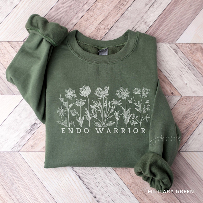 Pu&ograve; includere: Una felpa verde con un disegno floreale bianco e il testo "ENDO WARRIOR".