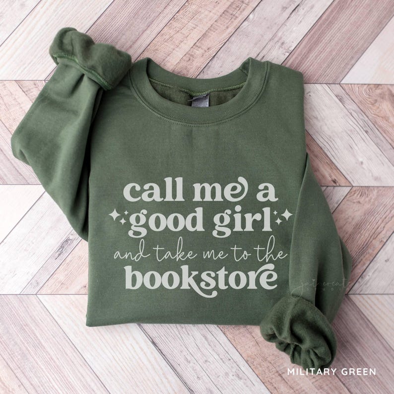 Może przedstawiać: Oliwkowozielona bluza z okrągłym dekoltem i białym napisem "call me a good girl and take me to the bookstore" oraz małymi czteroramiennymi gwiazdkami. Odzież posiada długie rękawy z prążkowanymi mankietami i prążkowanym dekoltem.
