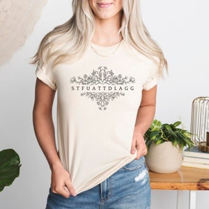 May include: A cream coloured t-shirt with a floral design and the text "STFUATTDLAGG" printed on the front.